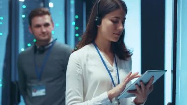 Yüksek odaklı bir kadın, bir veri merkezinde, kulaklık takarken dikkatle tablet kullanıyor.