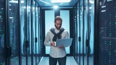 Bir bilişim uzmanı, modern, yüksek teknoloji veri merkezi ortamında bulunan bir dizüstü bilgisayar üzerinde gayretle çalışıyor.