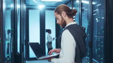 Son derece odaklanmış bir birey, modern ve gelişmiş bir veri merkezinde çalışırken bir dizüstü bilgisayar kullanıyor.