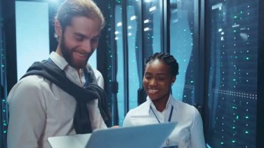 Bir sunucu odasında, iki profesyonel veri içgörülerini tartışarak, kendi alanlarında takım çalışmasının önemini vurgularlar