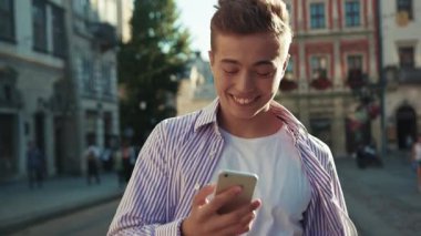 Yüzünüzü kapatın, mutlu adam sokakta yürüyün, etrafa bakın, gülümseyin, güneş ışığı, sevimli iş aleti, şehir dışındaki akıllı telefon teknolojisi, yavaş çekim, yakışıklı dokunmatik portre.