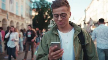 Gözlüklü şık genç adam telefon kullanıyor kulaklıkla müzik dinliyor mutlu bir cep telefonu ışığı gezici cihaz açık havada akıllı telefon teknolojisi yakışıklı hippi yavaş çekim portresini kapat