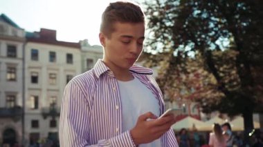Mutlu yüz genç adam sokakta duruyor telefon kullan kamera güneş ışığı mobil cihaz şehir dışında sms akıllı telefon teknolojisi yakışıklı dokunmatik yakın çekim portre yakın çekim