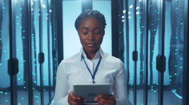 Odaklanmış bir kadın, modern teknolojinin özünü somutlaştıran yüksek teknoloji veri merkezinde bir tablet kullanıyor.