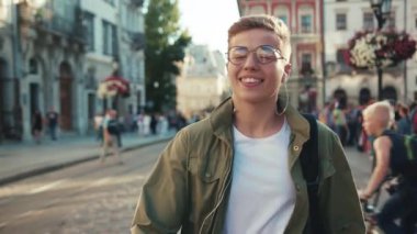 Yavaş çekim, gözlüklü genç adam sokakta dans ediyor kulaklıkla müzik dinliyor, cep telefonuyla gülümsüyor, cep telefonuyla geziyor açık havada geziyor akıllı telefon teknolojisi yakışıklı hippi portreyi kapatıyor.