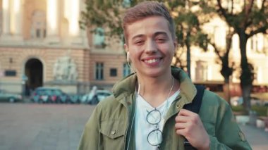 Kulaklıklı genç adam, kameraya bak. Gülümse. Sokakta mutlu ol. Güneş ışığı.