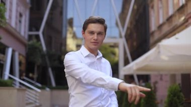 Genç yakışıklı işadamı kameraya bakıyor gülümseyerek iş merkezinin yanında dans ediyor başarılı mutlu patron yönetici yakışıklı ofisi kapatıyor ağır çekim tutkusuyla ayakta duruyor