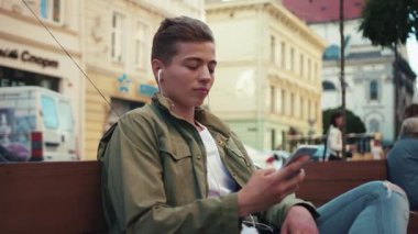 Çekici genç adam telefon kullanıyor. Kulaklıkla müzik dinliyor. Gülümsüyor, gülümsüyor.