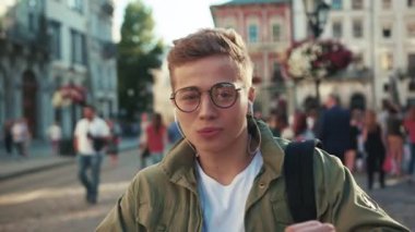 Gözlüklü genç adam sokakta dans ediyor kulaklıkla müzik dinliyor cep telefonuyla gülümsüyor cep telefonuyla geziyor mobil aletler açık havada akıllı telefon teknolojisi yakışıklı hippi yavaş çekimde portreyi kapat