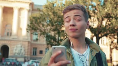 Kapat yüzünü yakışıklı genç adam cep telefonu kullan kulaklıkla konuş etrafına bak Steet City 'de yürü gülümse cep telefonu ışığı mutlu alet teknolojisi hipster yavaş çekim portresi