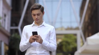 Ciddi anlamda başarılı bir iş adamı şehrin iş yeri caddesi cep telefonu Kafkasya şehir kurumsal şehir iş müdürü açık hava teknolojisi yürüyen yakışıklı cep telefonu dokunmatik ekranı üzerinde telefon kullanıyor.