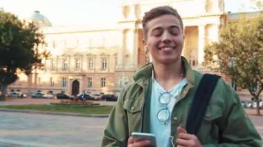 Genç, mutlu, yakışıklı bir genç telefon kullanıyor. Kulaklıkla müzik dinliyor. Etrafına bir bak.