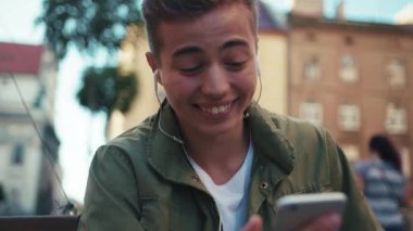 Kapat yüzünü genç adam telefon kullan kulaklıkla müzik dinle sokak gülüşüne otur mutlu cep telefonu mobil cihaz hippi yavaş çekim portresi