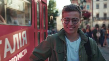 Kapalı yüzlü mutlu genç adam telefon kullan kulaklıkla müzik dinle arka planda cep telefonu tramvayı yürü mobil araç dışarıda yakışıklı hippi yavaş çekim portresi