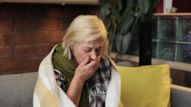Yalnız hasta kadın kameraya bakıp öksürüyor. Kanepede oturan, saray sarısı saçlı, renkli yastıklı, mutsuz bir kadın. Oturma odası. İçeride. Grip..