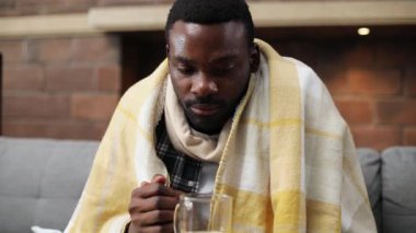 Çekici Afrikalı adam kanepeye oturmuş, sıcak çay içiyor. Yakışıklı, hasta bir gencin portresi. Yüksek ateş. Sıcaklık. Hastalık..