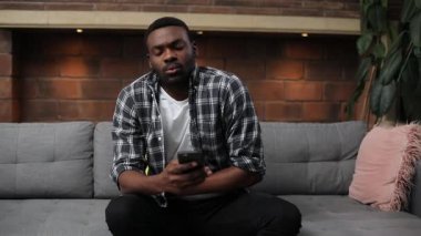 Kız arkadaşıyla mesajlaşan, kanepede oturan tatlı bir Afrikalı. Ekose gömlek giyen hasta bir gencin portresi. Karnım ağrıyor. Kapalı.