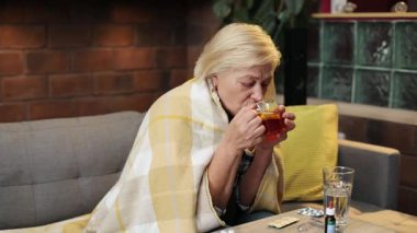 Kafkasyalı bir kadın elinde limonlu bir fincan sıcak çay, içiyor. Kanepede oturan mutsuz hasta büyükannenin portresi. Grip. Hastalık. Kapalı.