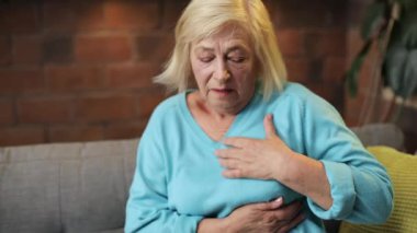 Sevimli büyükannem kanepede uzanıp kalbe dokunuyor. Mavi kazak giyen, kalbi ağrıyan beyaz bir kadın. İçeride. Hastalık. Oturma odası.