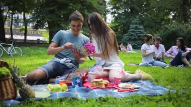 Uzun saçlı, erkek arkadaşının yanında oturan güzel bir esmer. Fotoğraf albümüne bayılan beyaz bir çift. Açık havada. Yaz zamanı. Gündüz vakti. Piknik.
