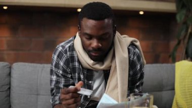 Kanepede oturup reçete okuyan tatlı Afrikalı adam. Elinde haplar tutan hoş bir gencin portresi. Tedavi için. Kapalı.