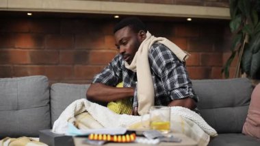 Ekose gömlek ve bej eşarp giyen çekici Afrikalı genç adam koltukta oturmuş, vücut ısısını ölçüyordu. Sevimli hasta bir adamın portresi. Kapalı.