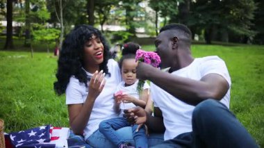 Beyaz tişörtlü yakışıklı bir adam kıza harika bir buket veriyor. Genç ve çekici Afrikalı kadın sevgili kocasını öpüyor. - Sürpriz. Romantik anlar. Günlük hayat. Yaz zamanı. Açık havada..