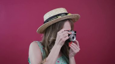 Saman kafalı güzel genç bir kadın retro kamerayla fotoğraf çekmek için doğru açıyı seçiyor, sonra da kameraya büyüleyici bir şekilde gülümsüyor. Pozitif duygular, hobi, favori mesleğin. Kadın portresi, renkli arkaplan