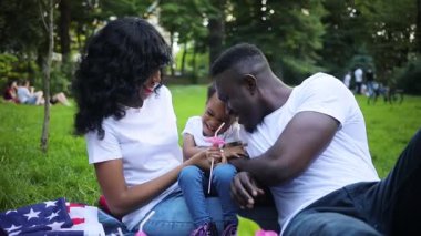 Mutlu eş, koca ve küçük kız şehir dışında tatillerini birlikte geçiriyorlar. Beyaz tişört giyen Afrikalı bir aile. Açık havada. Yaz zamanı. Park.