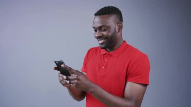 Şık giyinmiş çekici bir adam akıllı hatları aracılığıyla mesajlar atıyor. Mesajlara komik bir şekilde tepki veriyor. Gri bir arka planda neşe içinde gülüyor. Çevrimiçi olmak, teknolojiler, internette sörf. Erkek portresi, yakın görünüm