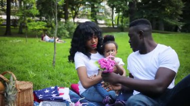 Yeşillik parkında piknik yapan hoş bir Afrikalı aile. Babam küçük güzel kıza bir buket pembe çiçek veriyor. Gençler battaniyeye oturuyor. Açık havada..