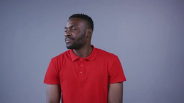 Kırmızı tişörtlü yakışıklı Afro-Amerikalı adam gri arka planda kameraya doğru gülümsüyor. Pozitif duygular, iyi hissetmek, eğlenmek. Erkek portresi, yakın görünüm