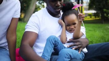 Şirin Afrikalı oyuncu kız babasının kucağında oturmuş gülüyor. Sarayda gülümseyen genç, siyah saçlı, kızına dokunan. Yakın plan. Mutlu çocukluklar. Yaz zamanı. Açık havada. Gündüz.