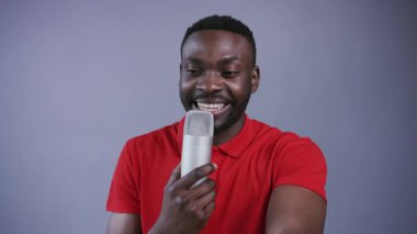 Şık gömlekli yakışıklı adam sahnede olduğu gibi mikrofon kullanıyor, izleyicilerle konuşuyor, espriler yapıyor, neşeli tepkiler veriyor, gri arka planda mutlu bir şekilde gülüyor. Joker, stand-up komedyeni, gösteri. Erkek portresi, yakın görünüm