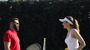 Erkek ve kadın tenis rakipleri birbirlerini tenis ağıyla selamlıyor, maçı tartışıyor, gülümsüyor ve flört ediyorlar, beşlik çakıyorlar. Başarı, aktif yaşam tarzı, spor için girin. Eğleniyorum..