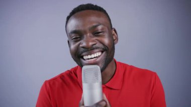 Gri arka planda mikrofonda şarkı söyleyen mutlu Afro-Amerikalı bir adam. Stüdyo, kayıt, hit, popülerlik. Olumlu duygular, neşeli ruh hali. Erkek portresi, yakın görünüm