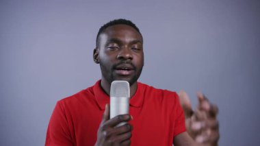 Yakışıklı Afro-Amerikalı şık gömlekli adam mikrofon kullanıyor, sunuyor, şaka yapıyor, gri arka planda izleyicilerle konuşuyor. Kulüp, gösteri, tiyatro. Erkek portresi, yakın görünüm