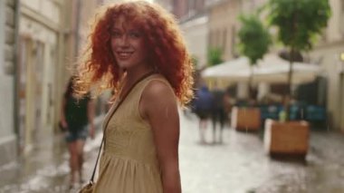NEW YORK - 5 Nisan 2017: Kırmızı kıvırcık saçlı, yağmurda yürüyen çekici bir kadın kameraya bakın mutlu bir gülümseme dönüyor sevimli moda su silueti yaz yüzü yalnız bir kadın