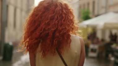 Kırmızı kıvırcık saçlı, tatlı bir kadın sokakta yağmurda yürüyor kameraya bakıyor mutlu bir gülümseme çeviriyor güzel bir portre moda su silueti yaz silueti kadın yalnız duruyor.