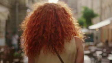 Kırmızı kıvırcık saçlı, gülümseyen genç bir kadın yağmur altında yürüyor. Kameraya bak. Mutlu moda su siluetini çeviriyor.