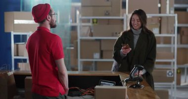 Postane çalışanı müşteri hizmetleri. Beyaz tenli, gülümseyen bir kadın için servis resepsiyonunda karton kutu veriyor. Halk ve işler.