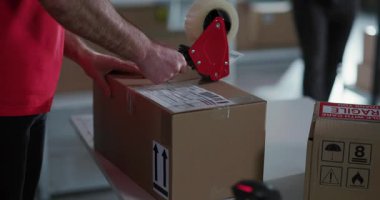 Kırmızı üniformalı iki orta yaşlı adamdan oluşan beyaz bir ekip posta deposundaki perakende kutuları toplayıp sıralıyorlar..