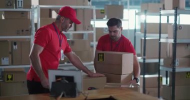 Kırmızı posta üniformalı birkaç depo çalışanı hızlı çalışarak paket kutularını toplayıp tarıyor. Takım çalışması. Görevler.