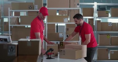 İşbirlikçi orta yaşlı erkek arkadaşlar kırmızı üniforma giyip iş konuşuyorlar ve teslimat paketlerini tarıyorlar. Takım çalışması. Halk ve işler.