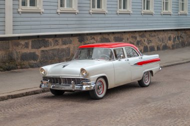 Kırmızı çatılı eski bir antika araba şehrin kaldırım taşı caddesi boyunca taştan temeli olan eski bir ahşap evin arka planına çarpıyor..