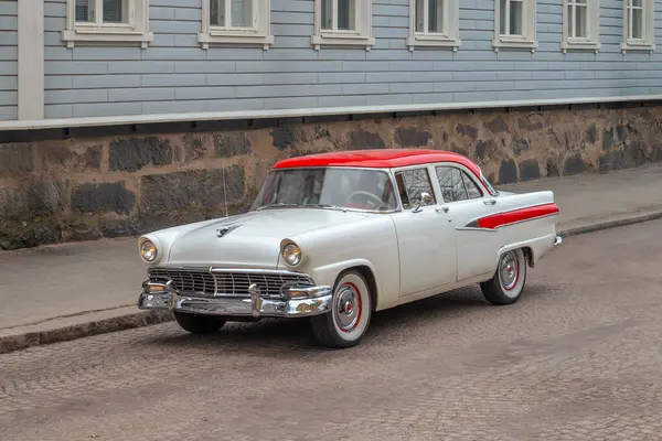 Kırmızı çatılı eski bir antika araba şehrin kaldırım taşı caddesi boyunca taştan temeli olan eski bir ahşap evin arka planına çarpıyor..