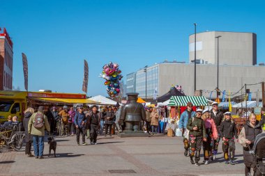 Şehir pazarı. Kış tatilinden sonra piyasada çalışmaya başlayacağım. Sert bir bronz polis memuru markette düzeni sağlar. Finlandiya, Oulu - 2025, 30 Nisan.