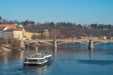 Şehrin geleneksel nehir mimarisi ve tarihi kemerli köprüsü ile Prag 'ın Vltava Nehri' ni gezen modern tur teknesi. Prag, Çek Cumhuriyeti - 18 Şubat 2025.