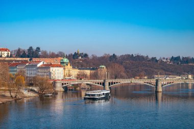 Panoramik Prag şehri: Majestic Castle, Vltava River, ve açık mavi gökyüzü altında bir tur teknesi olan tarihi Küçük Şehir. Prag, Çek Cumhuriyeti - 19 Şubat 2025.