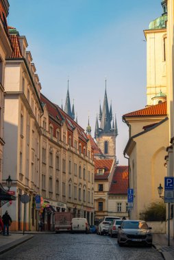 Tarihi Prag caddesi Tyn 'dan önce kilisemizin ikonik Gotik kulelerine çıkıyor. Geleneksel binalar, park edilmiş arabalar ve yayalar var. Prag, Çek Cumhuriyeti - 24 Şubat 2025.